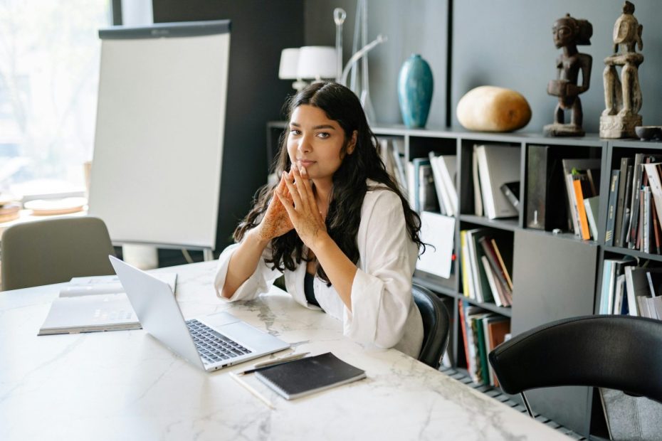 A businesswoman sitting at a marble table in a stylish office, working on a laptop.